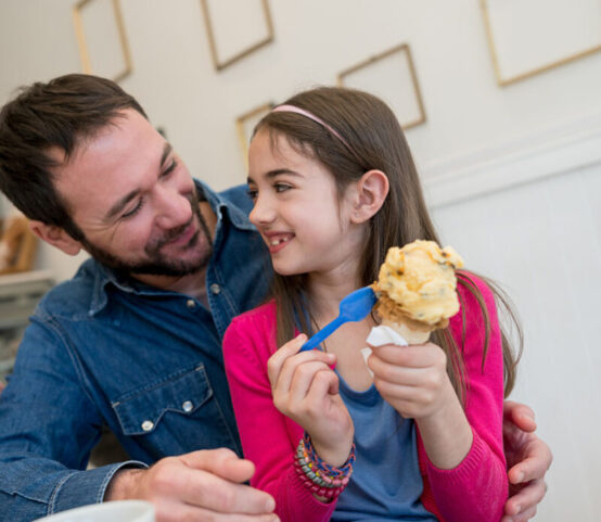 Dad and daughter enjoying an ice cream at the ice cream parlor both looking happy and smiling